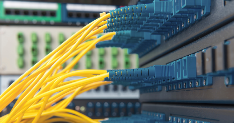 Yellow fiber optic patch cables connected to blue LC adapters on a network patch panel