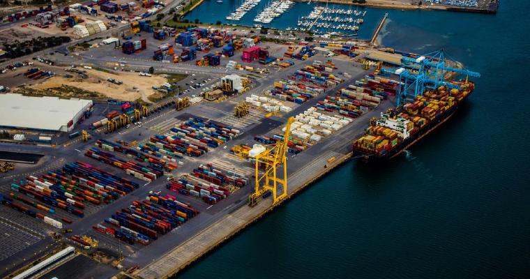 Aerial view of a container terminal, with thousands of containers stacked across the yard, a single ship alongside being loaded, and an idle crane on the quay